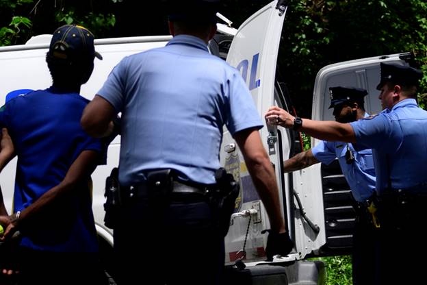 Three police officers are seen standing by a police van, with one officer appearing to guide a person inside. The image could be related to recovering lost property.